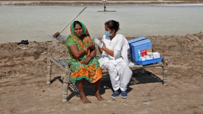 印度最西部的邦——古吉拉特邦苏仁德拉那加区的盐田，一名医护人员替一名妇女接种新冠疫苗。（图取自路透社）