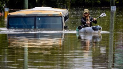 在布里斯班郊区米尔顿镇一条被淹的街道上，一辆巴士被洪水淹没，一名男子划著皮划艇避难。（图取自法新社）