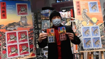 图为生肖邮票设计师、法籍华裔画家陈江洪在仪式现场展示邮票。（图取自中新社）