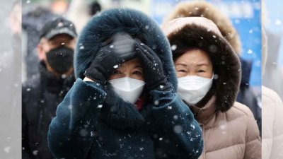 在韩国首尔中部，戴著口罩的通勤者本月17日在降雪期间行走的档案照。（图取自路透社）