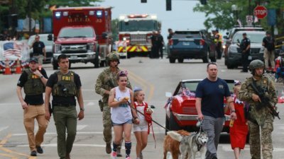 在伊利诺伊州芝加哥海兰帕克举行的7月4日游行发生枪击案后，执法人员护送一家人离开现场。（图取自法新社）
