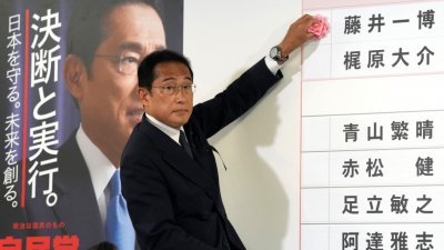 日本首相岸田文雄周日晚在自民党位于东京的总部，在候选人姓名板前给基本确定当选者的名字贴红花。（图取自法新社）