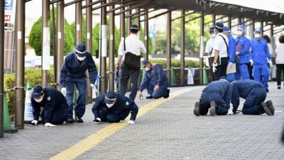 调查人员在奈良市安倍遇刺现场附近，俯下身子详细搜查地面，看能否找到子弹。（图取自共同社/路透社）
