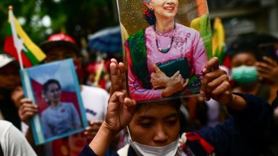 在泰国曼谷的缅甸大使馆外，示威者周二高举遭软禁的缅甸前国务资政昂山淑姬的照片，同时竖起象征反抗独裁的“三根手指”，抗议缅甸军政府处决民运人士。（图取自法新社）