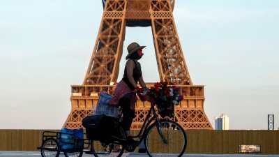 民众戴著口罩，骑著脚车经过法国首都巴黎的地标埃菲尔塔。（图取自路透社）