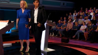 英国保守党党魁候选人特拉斯（左）与苏纳克于25日，站在英国广播公司（BBC）提供的辩论平台上，微笑著与现场观众打招呼。（图取自路透社）