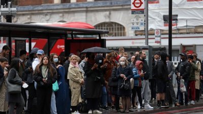 在伦敦维多利亚火车站，通勤者在一个巴士站等候巴士到来。（图取自法新社）