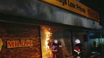 消拯员以铁锯开MR DIY店的铁卷门，以进入店内灭火。