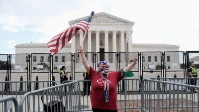 美国联邦最高法院周五推翻近50年前将堕胎合法化的标志性判例，一名示威者在美国最高法院外高举美国国旗。（图取自路透社）