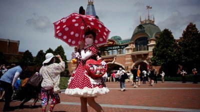 上海迪士尼乐园周四起恢复运营，一名精心打扮的游客戴上口罩，撑著粉红的伞出现在园区里。（图取自路透社）