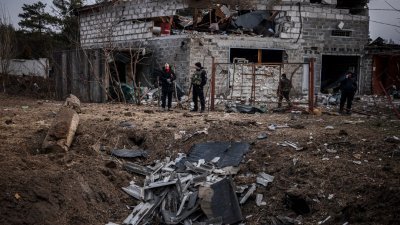 在基辅郊区的一所房屋前，警察和居民当地时间周六站在炮弹坑旁。俄军近日加强轰炸，目前距离基辅仅5公里。（图取自法新社）