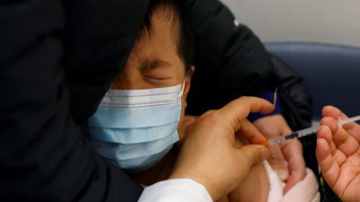香港一名3岁的儿童在接种新冠疫苗时，似乎有些害怕，被大人抱在怀中，紧闭双眼。（图取自路透社）