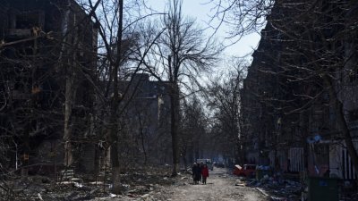 在被围困的乌克兰南部港口城市马里乌波尔，当地居民上周五在遭炮弹摧毁的住宅楼附近行走。（图取自路透社）