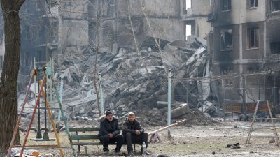 乌克兰南部港口城市马里乌波尔周五，民众坐在毁坏的居民楼前的长凳上。（图取自路透社）
