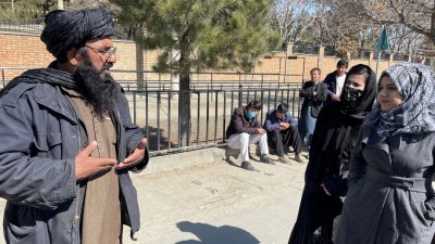 一名塔利班成员在喀布尔师范大学前与女学生讲话。（图取自路透社）