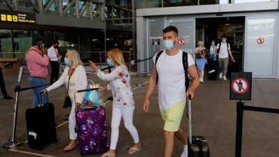戴著口罩的旅客拖著行李，走出西班牙马拉加机场大厅。（路透社档案照）