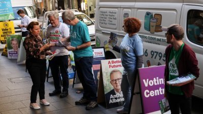 有民众于周二准备在澳洲悉尼中央商业区提前投票时，有竞选团志愿者在澳洲选举委员会提前投票中心入口处向选民派送传单拉票。（图取自路透社）