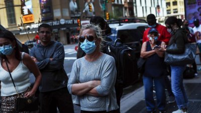 在纽约时报广场，一名戴著口罩的妇女在附近排队等候旅游巴士。（图取自路透社）