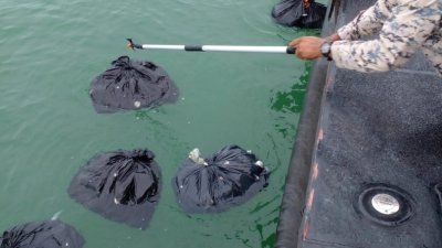 玻州港口海事执法机构捞起漂浮在海面的黑袋。