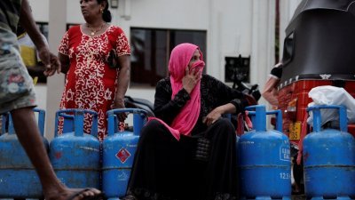 在斯里兰卡首都科伦坡，一名妇女与民众在经销商前排队购买煤气。（图取自路透社）
