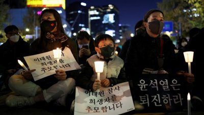 韩国民众上周六在首尔市政厅广场举行的烛光守夜活动中举著标语牌，除悼念梨泰院踩踏事故中的罹难者，也要求总统尹锡悦下台。（图取自路透社档案照）