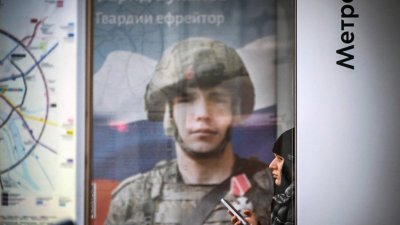 一名女子周二坐在展示俄军广告牌旁的公共汽车站。（图取自法新社）