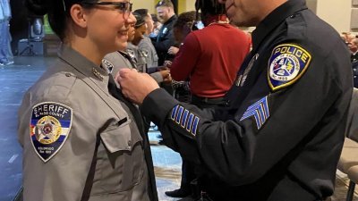 美国警察瓦尔迪维亚在22年前从毒窟中救出一名六周大的女婴，如今她已从警校毕业，由他亲自为她别上警徽。（图取自Escondido Police Department面子书）
