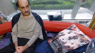 伊朗男子纳赛里坐在自己的“领地”和行李中，看着创作灵感取材于他本身遭遇、由好莱坞著名影星汤姆.汉克斯主演的电影《幸福终点站》海报。（法新社档案照）