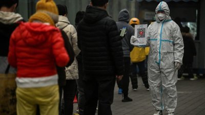 北京一名身著防护服的工作人员在核酸检测亭，引导正在排队的市民扫描电子健康码。（图取自法新社）