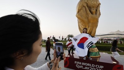 韩国球迷在多哈海湾球场外的大力神杯标志，拿著韩国国旗拍照留念。（图取自路透社）