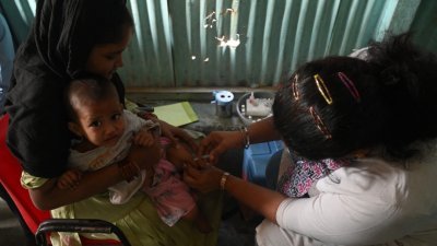 印度孟买麻疹爆发导致10名儿童死亡，一名卫生工作者周三在临时疫苗接种营地为一名儿童注射疫苗。（图取自法新社）