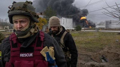 上周日，乌克兰赫尔松的一个石油储备遭到俄军袭击，黑烟升起，乌克兰一名救援人员和一名士兵在该地区进行检查。（图取自法新社）



