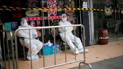 两名身穿防护服的人员上周六（26日），坐守在一个被围封的餐厅区外。（图取自路透社）