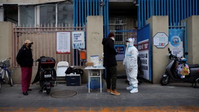 周日，北京居民在进入居民楼前，让防疫人员进行核酸检测。（路透社）
