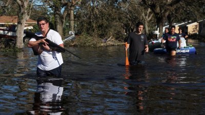 飓风“伊恩”给美国佛罗里达州带来严重淹水灾情，一名男子带上枪支，和家人带著家当搬离家园。（图取自路透社）