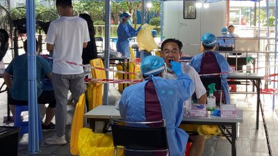 中国广东省深圳市爆发新一轮疫情，身著防护服的医护人员周五在南山区核酸检测点，为民众采集拭子。（图取自路透社）