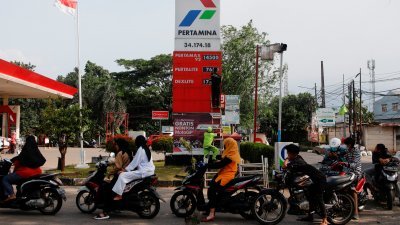 印尼国家石油公司加油站的工作人员，更换燃油价格，而现场已有大批摩哆排队添油。（图取自路透社）
