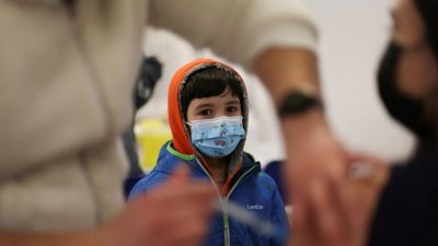 一名小孩在智利首都圣地亚哥的新冠疫苗接种中心，看著医护人员注射疫苗。（路透社档案照）