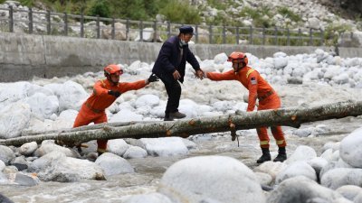 在四川甘孜州泸定县磨西镇，甘孜州森林消防支队康定中队队员周二在木桥旁护送灾民。 （图取自中新社）