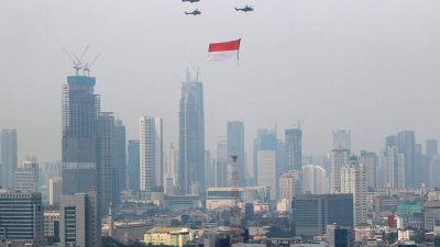 2021年8月17日，在雅加达举行的印尼第76届独立日庆祝活动期间，携带巨幅印尼国旗的印尼空军直升机在高层建筑上空飞行。（图取自路透社档案照）