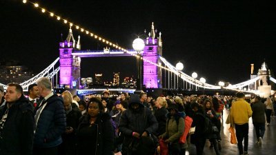 民众周五晚仍在排队轮候进入西敏宫瞻仰英女王灵柩。后方的伦敦塔桥被照上紫色灯光，以纪念上周驾崩的伊丽莎白二世。（图取自路透社）