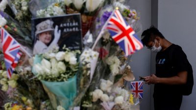 一名香港男子手持英国国旗，周一在英国驻香港总领事馆外排队吊唁英国女王伊丽莎白二世。（图取自路透社）