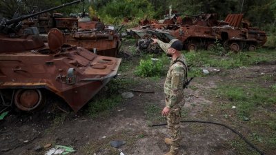 乌克兰军人在刚从俄军手中夺回的伊久姆镇，检查被摧毁的俄罗斯装甲运兵车。（图取自路透社）