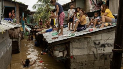 台风奥鹿于周日登陆菲律宾。周一，布拉干省圣米格尔的居民们在自家屋顶上等待台风带来的洪水消退。（图取自路透社）
