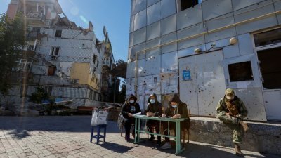 上周日，在乌克兰东南部马里乌波尔市，“顿涅茨克人民共和国”加入俄罗斯的公投的第3天，“选举委员会”成员在一栋被毁的住宅楼附近等待选民前来投票。（图取自路透社）