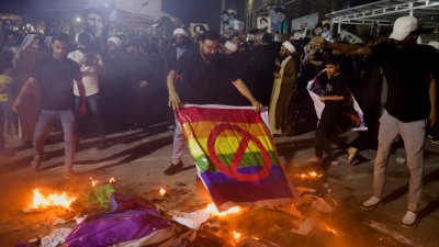 7月12日在伊拉克巴格达抗议亵渎《可兰经》的活动上，一名什叶派穆斯林焚烧象征LGBT群体的彩虹旗。（图取自路透社）