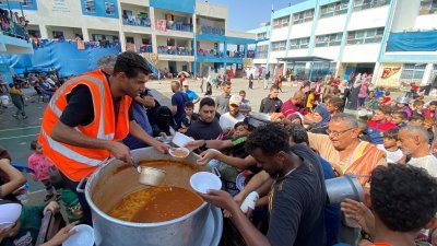 在加沙地带南部拉法，一所原本是联合国开办的学校目前已经成为避难所，志愿者10月23日向流离失所的巴勒斯坦人派发食物。（图取自路透社）
