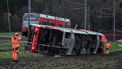 周五在瑞士首都伯尔尼西北部吕舍茨镇脱轨的列车车厢，侧翻在轨道旁的草地上，工作人员事发后在现场善后。（图取自法新社）