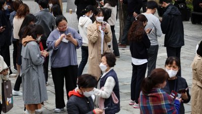 午休时间，上班族聚集在韩国首尔市立美术馆外，用手机查看Toss应用程式，希望赚取外快。（图取自路透社）