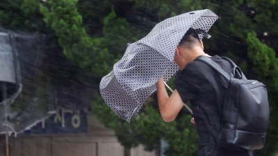 台风“卡努”周四登陆韩国南海岸。在东南部港口城市釜山，一名男子撑著被风雨吹歪的雨伞。（图取自韩联社/路透社）